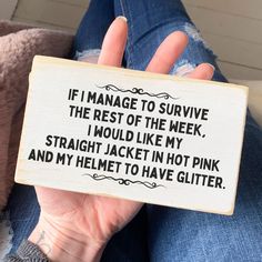 a person holding up a wooden sign that says i manage to survive the rest of the week, i would like my straight jacket in hot pink and my helmet to have glitter