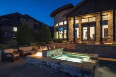 an outdoor hot tub lit up at night in front of a large house with patio furniture