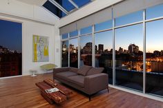 a living room filled with furniture and large windows overlooking the city at night, in front of a flat screen tv