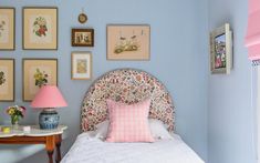 a bedroom with blue walls and pictures on the wall above the bed, along with a pink lamp