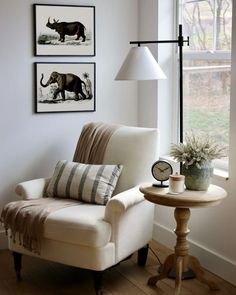 a white chair sitting in front of a window next to a lamp and pictures on the wall