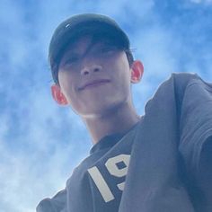 a young man wearing a hat and holding a cell phone up to his ear with the sky in the background