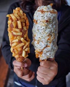 a person holding two different types of food in their hands, one is covered with cheese and the other has french fries