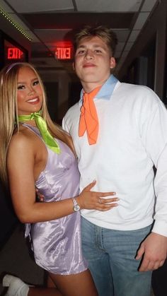 a man standing next to a woman in a purple dress and orange neck tie at an event