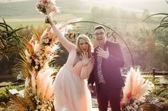 a man and woman standing next to each other in front of an arch with flowers