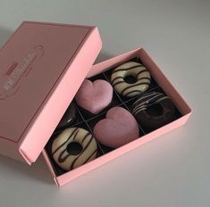 a pink box filled with donuts covered in frosting and heart shaped candies