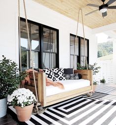 a porch swing with potted plants on it and a black and white striped rug