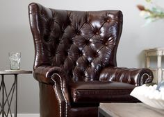 a brown leather chair sitting in a living room next to a coffee table and vase