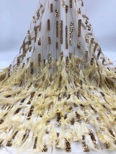 a white dress with gold sequins and feathers on the bottom is shown in front of a white background