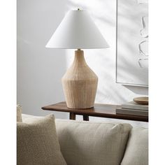 a table lamp sitting on top of a wooden table next to a white wall and couch