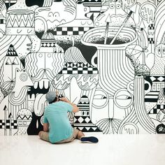 a person sitting on the ground in front of a wall with black and white designs