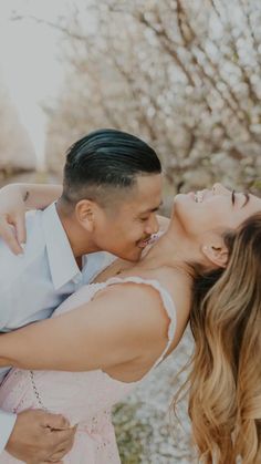 a man and woman kissing each other in the middle of an outdoor area with trees