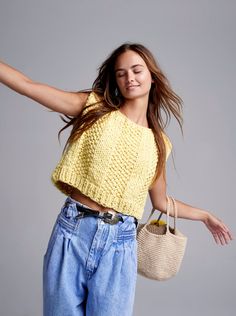 a woman in jeans and a yellow top is holding a handbag while posing for the camera