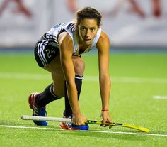 a female field hockey player crouching down to pick up the ball