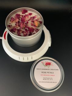 a bowl of rose petals is next to a container of soap on a black surface