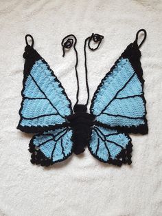 a crocheted blue and black butterfly on a white blanket with two strings attached to it