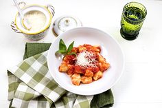 a white bowl filled with pasta and sauce on top of a green napkin next to two glasses