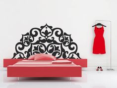 a red bed in front of a white wall with a black design on the headboard