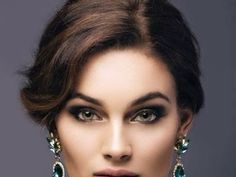 a woman with dark makeup and green jewelry