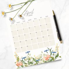 a calendar with flowers on it next to a pen and some daisies in the background