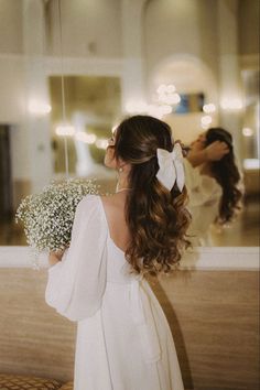 a woman standing in front of a mirror holding a bouquet of white baby's breath