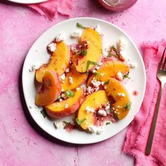 a white plate topped with sliced peaches on top of a pink cloth next to a fork