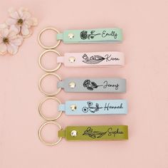 four keychains with names on them sitting next to a white flower and pink background