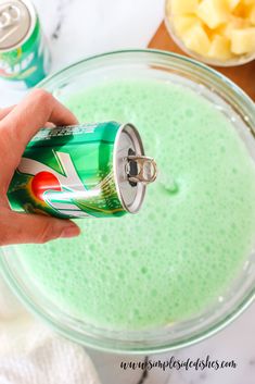 a hand holding a can of soda over a bowl of green liquid