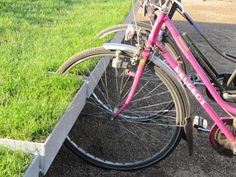 a pink bike parked next to a curb on the side of a road with grass