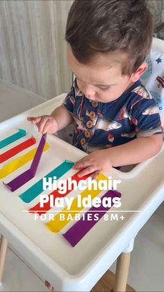 a little boy that is sitting in a highchair playing with some colored sticks