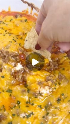 a person dipping a tortilla chip into a casserole dish with cheese and meat