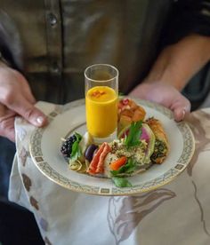 a person holding a plate with food on it and a glass of orange juice in the middle