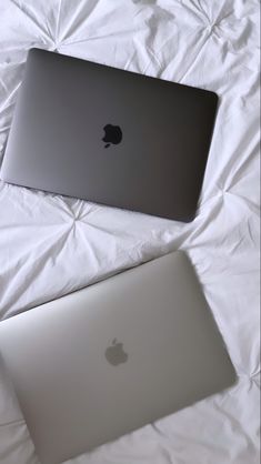 two apple laptops sitting side by side on a white bed sheet, one is silver and the other is black