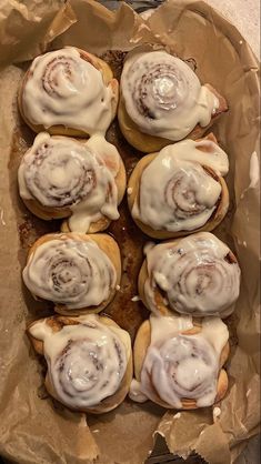 there are many cinnamon rolls with icing on top of each other in a paper bag