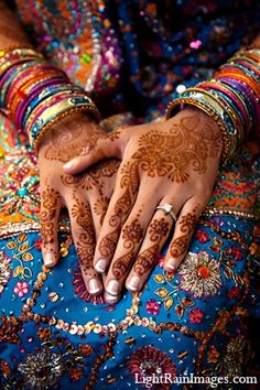 a woman's hands with henna tattoos and bracelets on her arm, holding onto