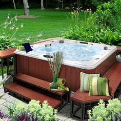 an outdoor hot tub surrounded by plants and flowers in the garden with benches around it