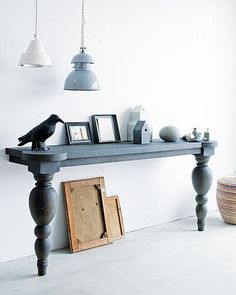 a black bird sitting on top of a wooden table next to a lamp and pictures