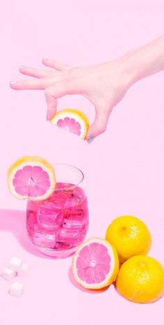 a hand reaching for some lemons in a glass filled with water and ice cubes