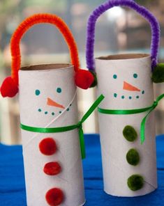 two snowmen made out of toilet paper sitting on top of a blue table cloth