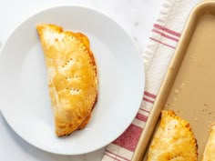 a piece of pastry on a plate next to a baking pan with some pastries in it