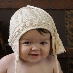 a baby wearing a white knitted hat with tassels on it's head