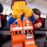 a lego man is standing in front of some other people wearing orange vests and hats