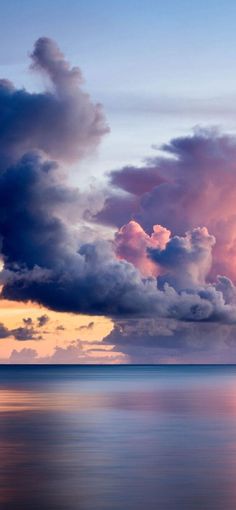 an airplane is flying in the sky over the ocean at sunset with clouds reflecting on the water