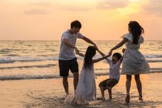 a group of people standing on top of a beach next to the ocean at sunset