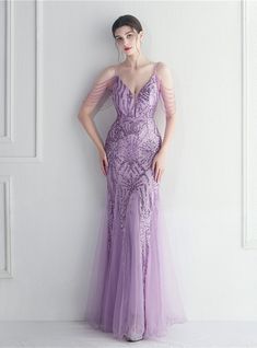 This purple mermaid prom dress is a spectacle of modern elegance, curated for grand prom nights, majestic balls, and formal soirees. The patterned sequins embellished on the mesh v-neck bodice sparkle as they catch light, supported gracefully by spaghetti straps. The zipper-up back ensures a flattering fit, while the tassel cap sleeves add a touch of playful sophistication. The beading adornments are a nod to meticulous craftsmanship, adding layers of luxury. The tulle skirt glides over the hips, elegantly making its way to the floor, showcasing a silhouette that is nothing short of glamorous. Purple Mermaid Prom Dress, Tulle Tutu Dress, Beaded Mermaid, Fishtail Maxi Dress, Beaded Party Dress, Purple Mermaid, Mermaid Sequin, Ladies Accessories, Tulle Tutu