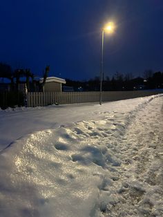 a street light shines brightly in the dark sky above snow - covered sidewalk and fence