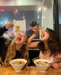 two women eating noodles with chopsticks at a restaurant