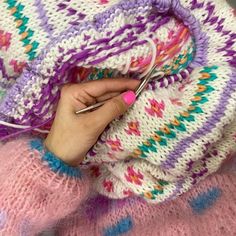 a woman is knitting with her hands on the end of a blanket that has been crocheted