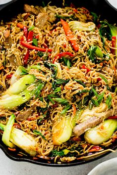 stir fried noodles with vegetables and meat in a skillet on a white counter top