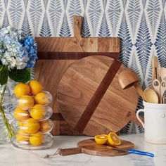 a wooden cutting board sitting on top of a counter next to vases and utensils